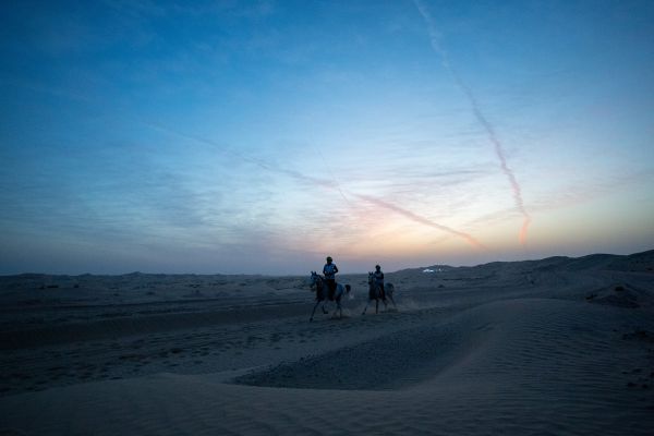 Two endurance riders crossing the Butheeb desert beneath a blue dawn sky